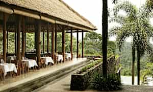 En utendørsrestaurant med stråtak og dekkede bord, omgitt av frodig grøntområder. (AI-generert tekst)