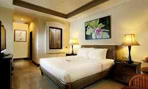 Et soverom med en stor seng, to nattbordslamper og et dekorativt bilde på veggen. (AI-generert tekst)