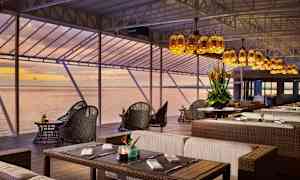 En restaurant med sitteplasser i rottingmøbler og utsikt over havet ved solnedgang. (AI-generert tekst)