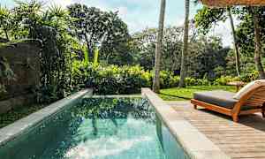 Bilde av et basseng med klart vann omgitt av frodig vegetasjon og en solseng på en treterrasse. (AI-generert tekst)