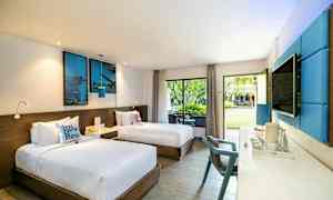 Et hotellrom med to enkeltsenger, moderne innredning med blå detaljer, og store vinduer som vender mot en hage. (AI-generert tekst)