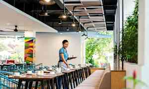 Et restaurantlokale med bord og stoler, der en person bærer et brett med kopper. (AI-generert tekst)