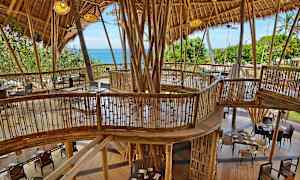 Bygning med bambuskonstruksjon og møbler, med utsikt over grøntområder og havet. (AI-generert tekst)