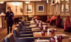 En restaurant med dekkede bord, røde glass og mørke stoler vises på bildet. (AI-generert tekst)