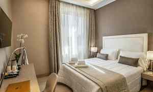 Et hotellrom med en dobbeltseng med hvitt og beige sengetøy, en skrivebord med lampe og en veggmontert TV. (AI-generert tekst)