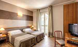 Et hotellrom med to enkeltsenger, en skrivebordshjørne og et stort vindu som slipper inn dagslys. (AI-generert tekst)