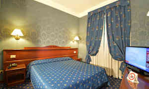 Et hotellrom med blå innredning, inkludert seng, gardiner og tapet, samt en TV ved siden av. (AI-generert tekst)