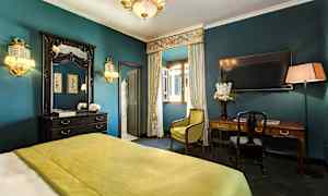 Et elegant innredet hotellrom med grønt sengeteppe, skrivebord, speil og gardiner foran et åpent vindu. (AI-generert tekst)