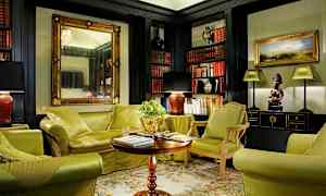 Et elegant innredet stue med grønne møbler, et salongbord og bokhyller fylt med bøker. (AI-generert tekst)