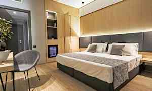 Hotellrom med dobbeltseng, nattbord og en stol ved et bord. (AI-generert tekst)