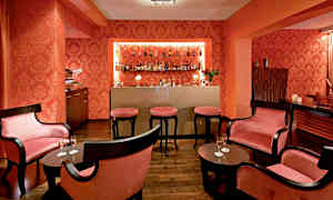 Bilde som viser et elegant område innredet som en cocktailbar med mørke møbler, rosa puter og flasker på en hylle. (AI-generert tekst)