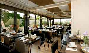 En lys restaurant med oppdekkede bord, dekorert med blomster og vinduer som viser en utendørs omgivelse. (AI-generert tekst)