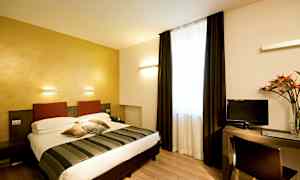 Et hotellrom med en dobbeltseng, skrivebord og TV. Rommet har lyse vegger og et stort vindu med mørke gardiner. (AI-generert tekst)