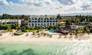 Strand med klart vann, parasoller og solsenger, omgitt av hotell og grøntområder. (AI-generert tekst)