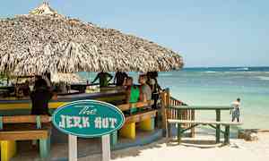 En strandbar med stråtak og et skilt som sier "The Jerk Hut". Havet er synlig i bakgrunnen. (AI-generert tekst)