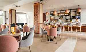 Et moderne innredet kafé eller bar med bord og stoler i forskjellige farger samt en opplyst bardisk i bakgrunnen. (AI-generert tekst)