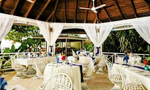 En utendørsrestaurant med hvitmalte møbler under et tretak. (AI-generert tekst)