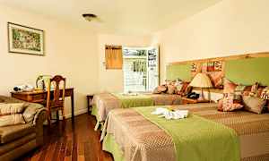 Et hotellrom med to enkeltsenger, en sofa, et skrivebord og en stol. Det er også en dør som fører til en balkong. (AI-generert tekst)