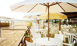 En strandbar med parasoller og hvite bord og stoler. (AI-generert tekst)