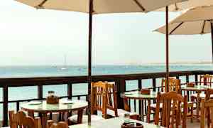 Utendørsbord og stoler under parasoller med utsikt mot havet. (AI-generert tekst)