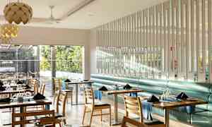 En moderne og lys restaurantinteriør med bord og stoler, hvor vinduer vender mot et frodig utendørsområde. (AI-generert tekst)