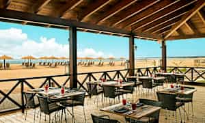 Restaurant med uteservering og utsikt over en strand med solsenger og parasoller. (AI-generert tekst)