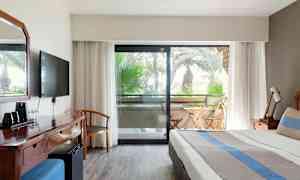 Bilde av hotellrom med seng, skrivebord og balkong med utemøbler. (AI-generert tekst)