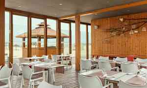 Restaurant med trepanel og glassvegger med utsikt over stranden. (AI-generert tekst)