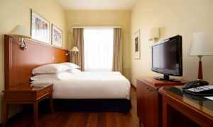 Hotellrom med en dobbeltseng, skrivebord, TV og store vinduer med gardiner. (AI-generert tekst)