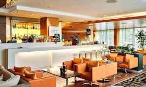 En moderne og elegant lounge med en hvit bardisk, bakgrunnsbelyste brennevinsflasker og komfortable oransje lenestoler. (AI-generert tekst)
