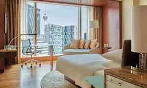 Et moderne hotellrom med vinduer som viser utsikt over en by, inkludert en tårnstruktur. (AI-generert tekst)