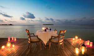 Et bord med to stoler står på en trebrygge ved vannet, omgitt av tente lys. (AI-generert tekst)