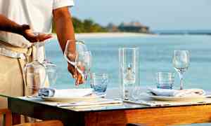 Restaurantpersonale som dekker et bord med vinglass ved en strand. (AI-generert tekst)