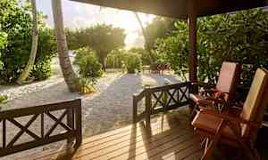 Utsikt fra en veranda med to solsenger, trær og sand i solnedgangslys. (AI-generert tekst)