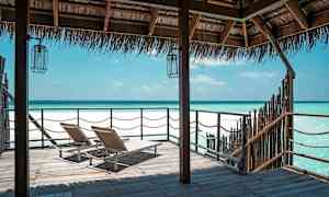 To solsenger på en trebro med utsikt over en klarblå kyst under et stråtak. (AI-generert tekst)