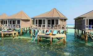 Bildet viser bungalower på stolper over klart vann, med solsenger på en terrasse. (AI-generert tekst)