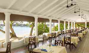 En restaurantterrasse med dekkede bord, omgitt av søyler og utsikt over stranden og vannet. (AI-generert tekst)