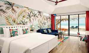 Et hotellrom med en dobbeltseng, sofa og en stor glassdør som vender mot en strand med palmer og havutsikt. (AI-generert tekst)