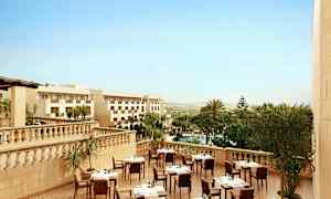 Hotellets utendørs terrasse med dekkede bord, omgitt av palmer og utsikt over landskapet. (AI-generert tekst)