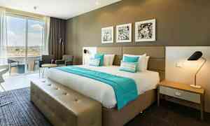 Hotellrom med en dobbeltseng, sitteområde og store vinduer. (AI-generert tekst)