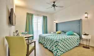 Et hotellrom med en dobbeltseng, dekorative puter og et bord med to stoler. (AI-generert tekst)