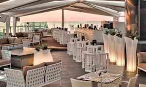 En lounge med moderne møbler, bord, sofaer og en bardisk under et overdekket tak. (AI-generert tekst)