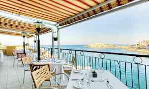 Et bord på en utendørsterrasse under en markise med utsikt over havet. (AI-generert tekst)