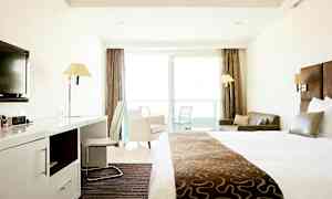 Et hotellrom med en stor seng, skrivebord, stol, sofa og balkong med glassdører. (AI-generert tekst)