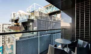 En balkong med moderne innredning, inkludert et rundt bord og stoler, med utsikt over en bygning med glass- og metallfasader. (AI-generert tekst)