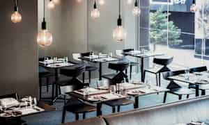 En moderne restaurant med elegant dekkede bord og hengende lyspærer. (AI-generert tekst)