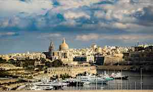 Utsikt over en by med en kuppelformet bygning og båter i en havn. (AI-generert tekst)