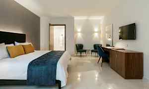 Hotellrom med dobbeltseng, skrivebord, to lenestoler og vegghengt TV. (AI-generert tekst)