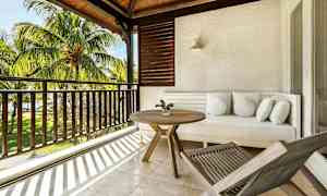 En terrasse med en hvit sofa, et rundt trebord og en solseng, med utsikt over palmer og grøntområde. (AI-generert tekst)