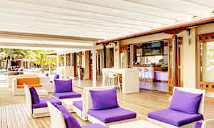 En uteservering med lilla puter på lenestoler og et barområde i bakgrunnen. (AI-generert tekst)